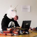 Un homme avec une tête de licorne devant un ordinateur et un tas de briques internet