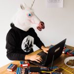 Un homme avec une tête de licorne devant un ordinateur et un tas de briques internet